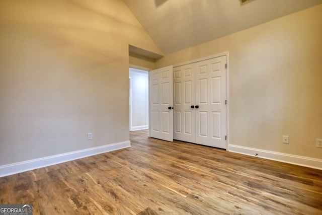 unfurnished bedroom with wood-type flooring, high vaulted ceiling, and a closet