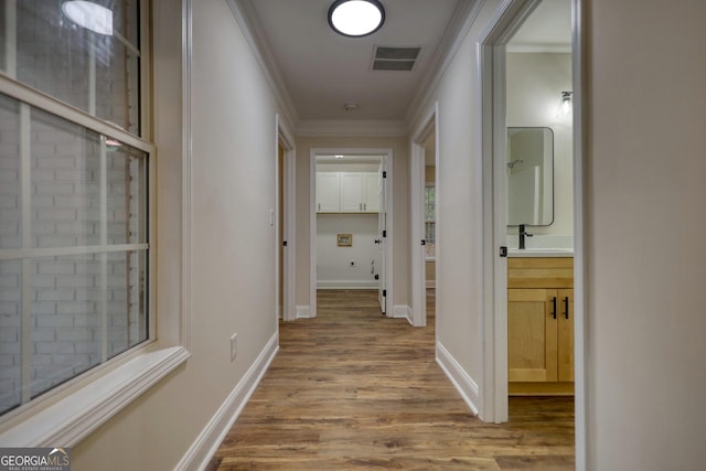 hall featuring light wood-type flooring, crown molding, and sink