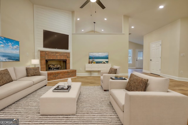 living room featuring a brick fireplace, light hardwood / wood-style floors, high vaulted ceiling, and ceiling fan