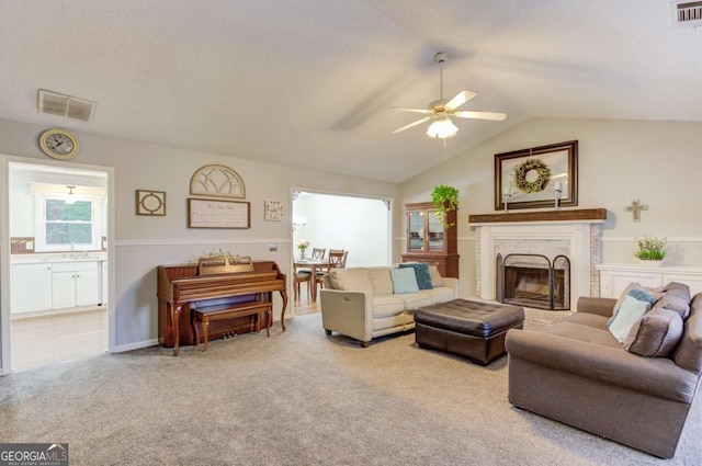 carpeted living room featuring a fireplace, vaulted ceiling, sink, and ceiling fan