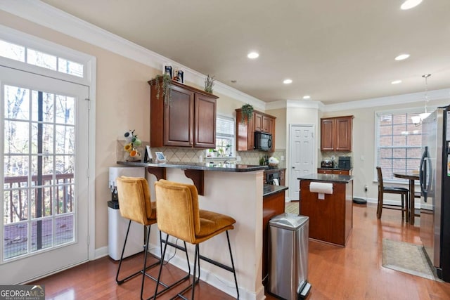 kitchen with a breakfast bar, a center island, kitchen peninsula, wood-type flooring, and stainless steel refrigerator