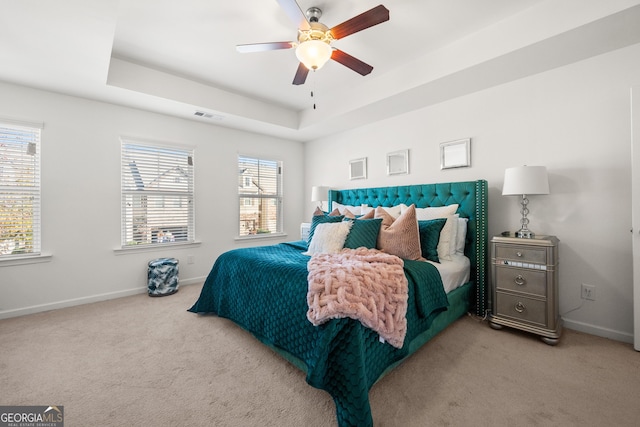 bedroom with ceiling fan, a raised ceiling, and light carpet