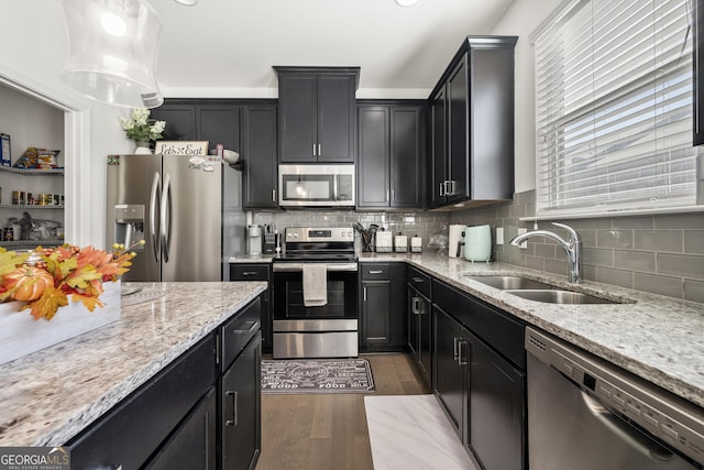 kitchen with sink, dark wood-type flooring, light stone counters, pendant lighting, and appliances with stainless steel finishes