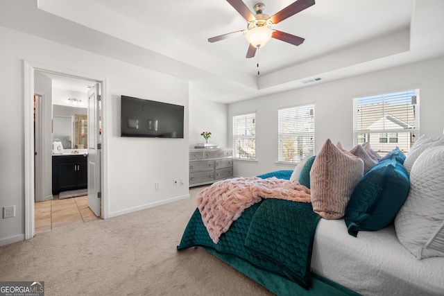 carpeted bedroom featuring a raised ceiling, ensuite bathroom, and ceiling fan