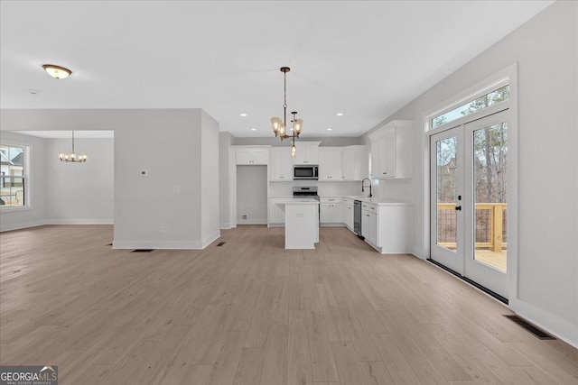 kitchen featuring french doors, appliances with stainless steel finishes, a notable chandelier, a kitchen island, and white cabinetry