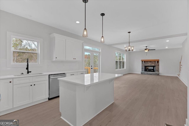 kitchen featuring backsplash, stainless steel dishwasher, sink, a fireplace, and white cabinetry