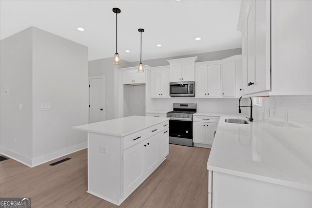 kitchen with appliances with stainless steel finishes, sink, a center island, white cabinetry, and hanging light fixtures