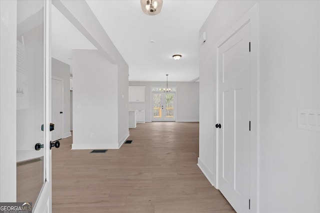 hallway featuring a chandelier, french doors, and light wood-type flooring