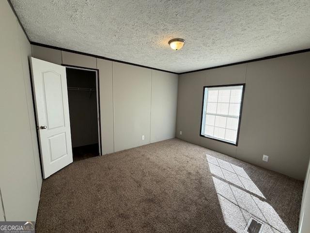 unfurnished bedroom featuring dark colored carpet, a textured ceiling, and a closet