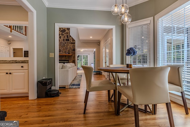 dining area with a fireplace, light wood-type flooring, and crown molding