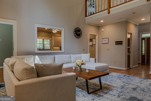 living room with crown molding, ceiling fan, a high ceiling, and light wood-type flooring