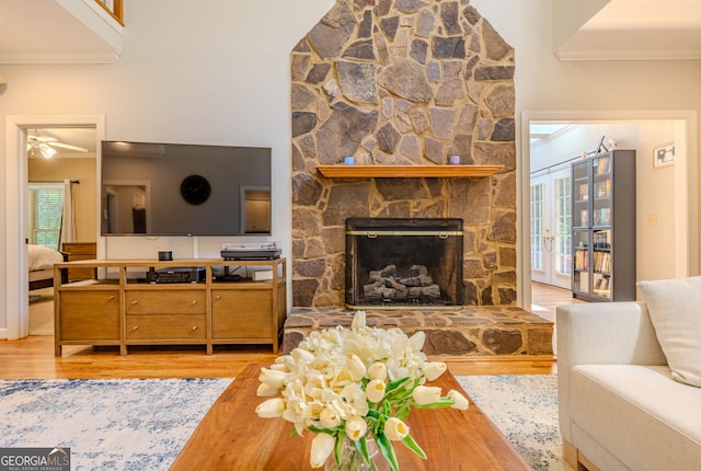 living room featuring a stone fireplace, ceiling fan, light hardwood / wood-style floors, and ornamental molding