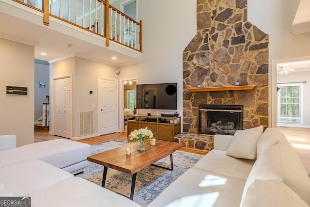 living room featuring ceiling fan, light wood-type flooring, a fireplace, and a high ceiling