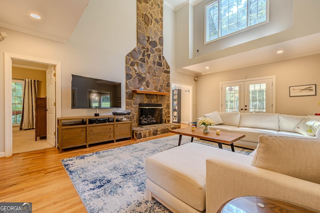 living room with french doors, crown molding, a towering ceiling, wood-type flooring, and a fireplace