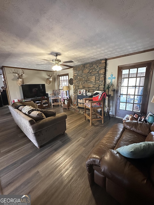 living room featuring a textured ceiling, dark hardwood / wood-style floors, a stone fireplace, and ornamental molding