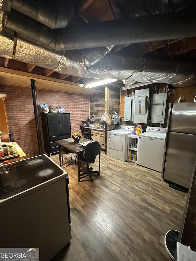 basement with brick wall, independent washer and dryer, electric panel, stainless steel fridge, and hardwood / wood-style floors