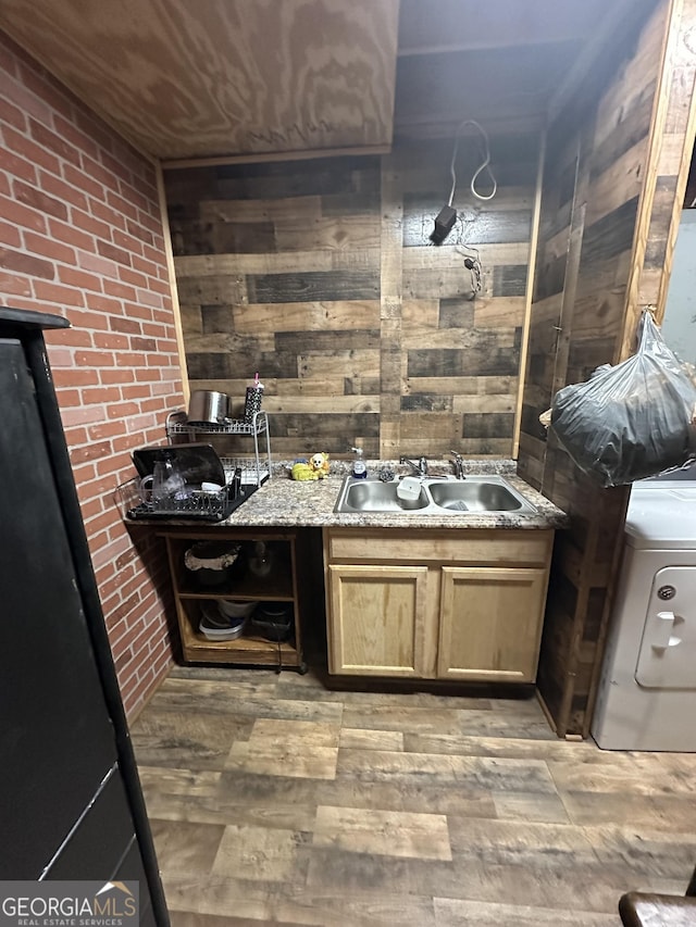 kitchen with sink, hardwood / wood-style flooring, light stone countertops, washer / dryer, and brick wall