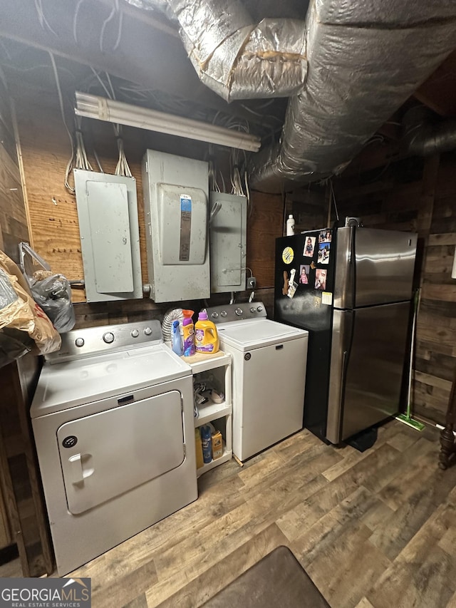 washroom with hardwood / wood-style floors, wood walls, washing machine and dryer, and electric panel