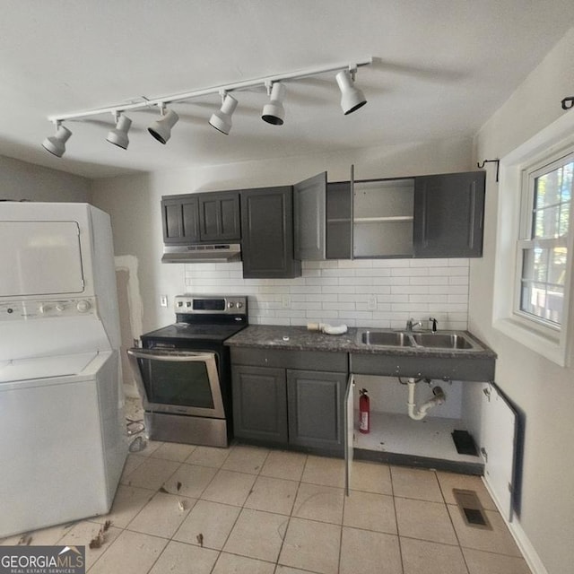 kitchen with rail lighting, tasteful backsplash, electric stove, stacked washer and clothes dryer, and light tile patterned flooring