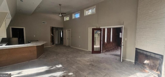 unfurnished living room with ceiling fan, a fireplace, and a high ceiling