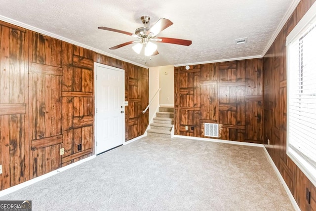 unfurnished bedroom with a textured ceiling, crown molding, multiple windows, and wooden walls