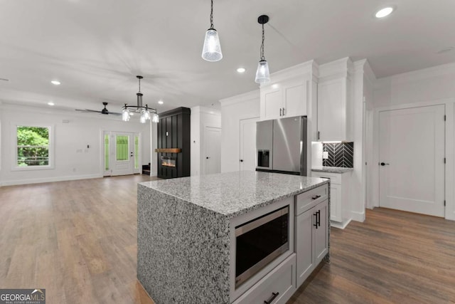 kitchen featuring a center island, appliances with stainless steel finishes, decorative light fixtures, light stone counters, and white cabinetry