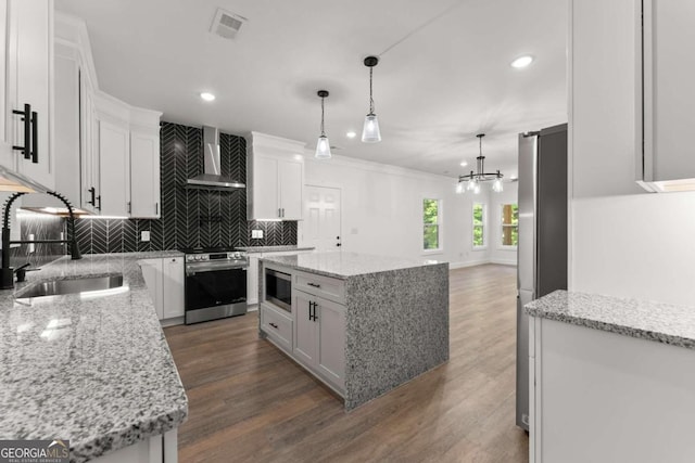 kitchen with white cabinets, a kitchen island, wall chimney range hood, and stainless steel appliances