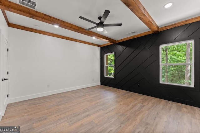 spare room featuring beam ceiling, wooden walls, plenty of natural light, and light hardwood / wood-style floors