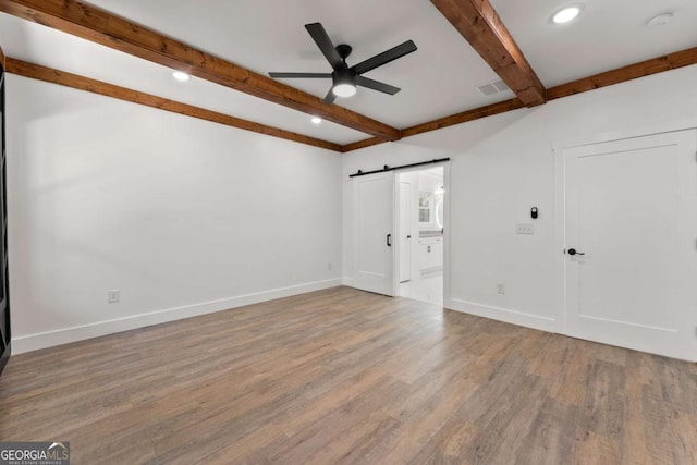 empty room with beamed ceiling, a barn door, hardwood / wood-style flooring, and ceiling fan