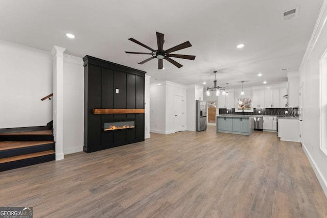 unfurnished living room featuring ceiling fan, ornamental molding, a fireplace, and light hardwood / wood-style flooring