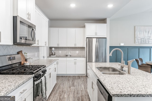 kitchen with a center island with sink, sink, white cabinetry, light stone countertops, and appliances with stainless steel finishes