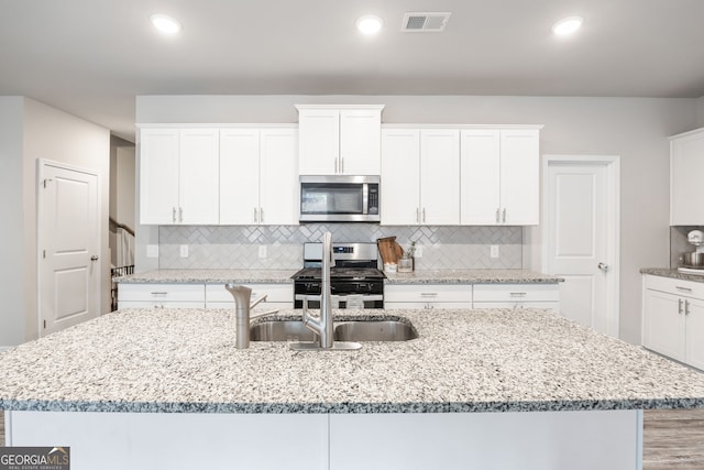 kitchen with light stone countertops, appliances with stainless steel finishes, and a kitchen island with sink