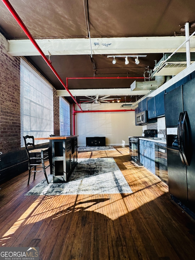 kitchen with black appliances, wood-type flooring, and brick wall