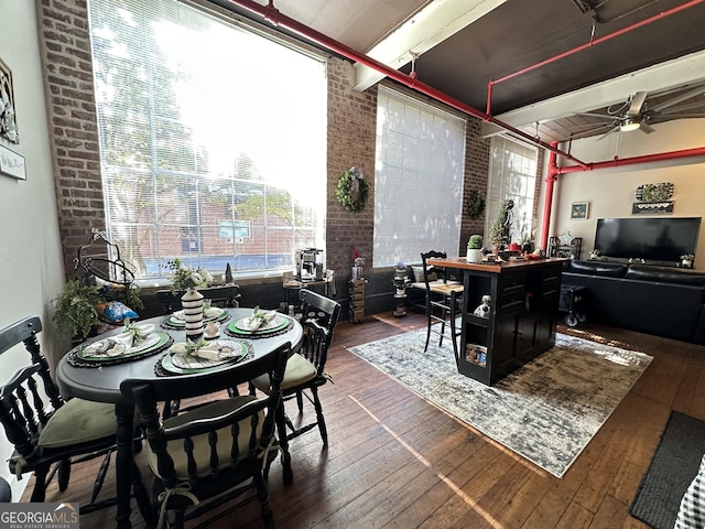 dining area with dark hardwood / wood-style floors, ceiling fan, and brick wall