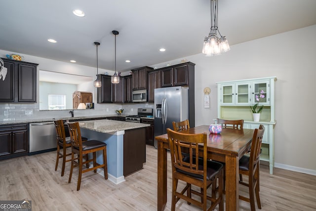 kitchen with pendant lighting, light hardwood / wood-style floors, a kitchen island, a kitchen bar, and stainless steel appliances