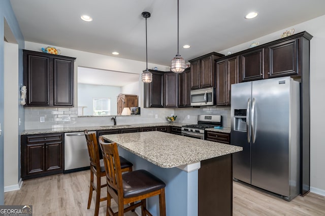 kitchen featuring light wood-type flooring, stainless steel appliances, sink, pendant lighting, and a kitchen island