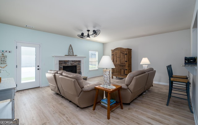 living room featuring a stone fireplace, ceiling fan, and light hardwood / wood-style floors