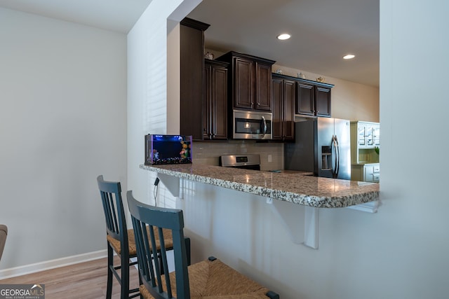 kitchen with kitchen peninsula, a kitchen breakfast bar, decorative backsplash, stainless steel appliances, and light hardwood / wood-style floors