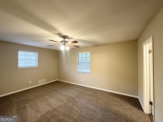 spare room featuring a textured ceiling, dark carpet, and a wealth of natural light