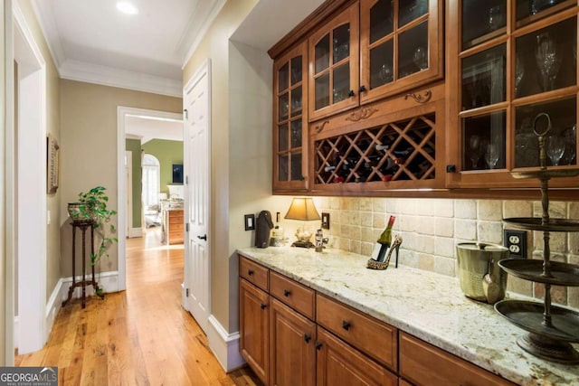 bar featuring light stone countertops, decorative backsplash, light wood-type flooring, and ornamental molding