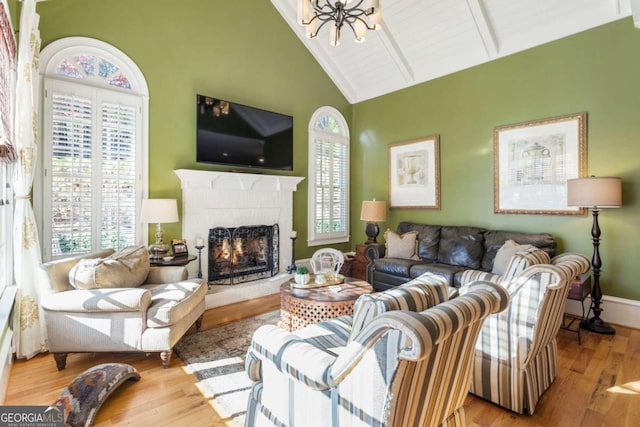 living room featuring an inviting chandelier, high vaulted ceiling, light hardwood / wood-style flooring, beamed ceiling, and a fireplace