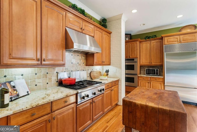 kitchen featuring light stone countertops, stainless steel appliances, backsplash, light wood-type flooring, and ornamental molding