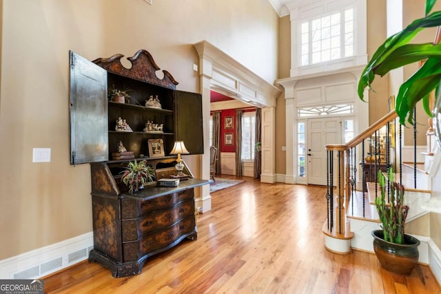 entrance foyer with a towering ceiling, light hardwood / wood-style floors, and ornamental molding