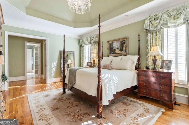 bedroom featuring a notable chandelier, light wood-type flooring, ornamental molding, and a tray ceiling