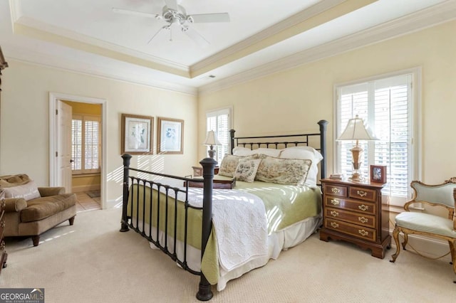 carpeted bedroom with ensuite bath, ceiling fan, a raised ceiling, and multiple windows