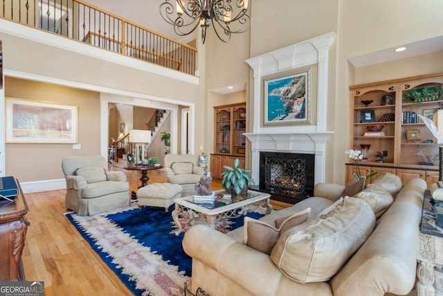 living room with hardwood / wood-style flooring, a towering ceiling, a high end fireplace, and a chandelier