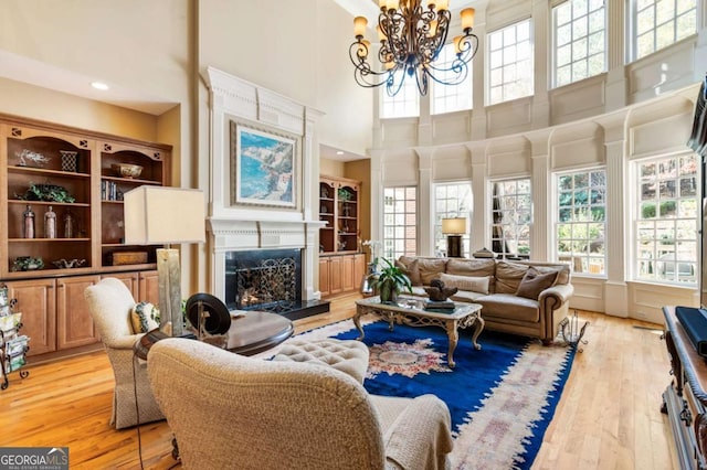 living room featuring a high end fireplace, a wealth of natural light, a towering ceiling, and light hardwood / wood-style floors