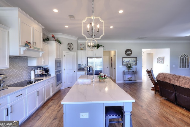 kitchen featuring pendant lighting, stainless steel appliances, a kitchen island with sink, white cabinets, and sink