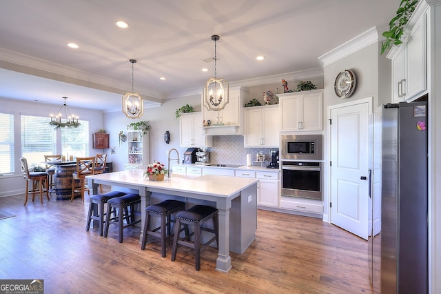 kitchen with an island with sink, appliances with stainless steel finishes, hanging light fixtures, and white cabinetry