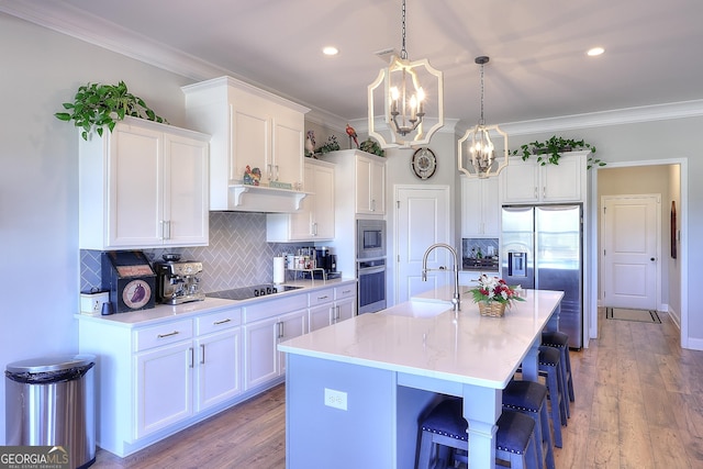 kitchen featuring stainless steel appliances, a kitchen island with sink, backsplash, white cabinets, and sink